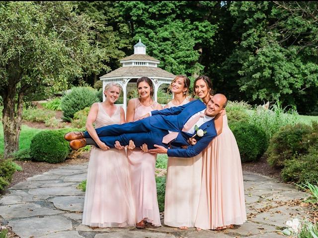 bridesmaids holding groom up sideways in front of gazebo